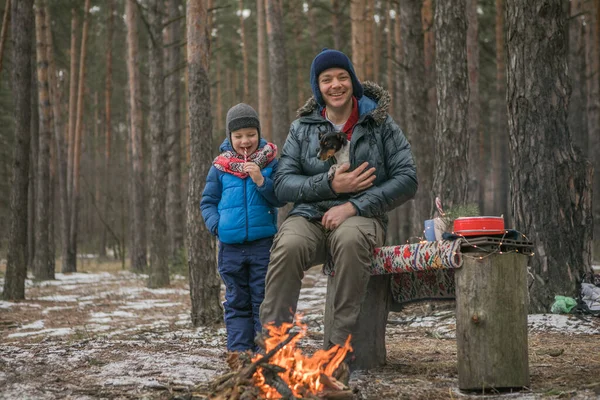 Happy family near the fire on a walk outdoors in sunny winter forest, Christmas holidays, father and son play together