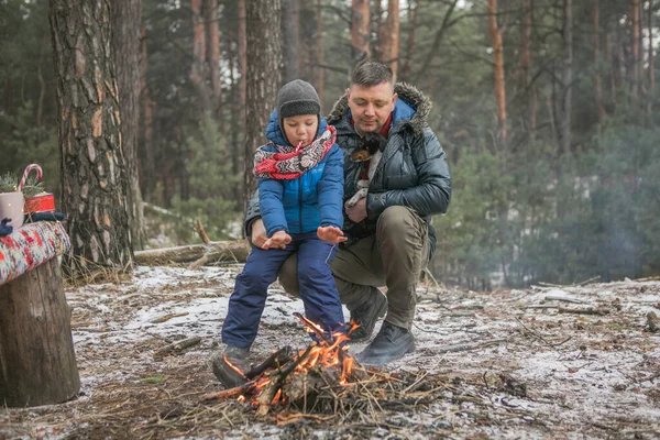 Happy family near the fire on a walk outdoors in sunny winter forest, Christmas holidays, father and son play together