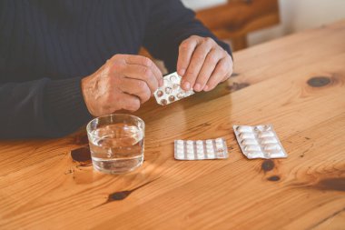 Yaşlı adamın elleri bir bardak su, sağlık ve tıbbi konsept içeren hapları topluyor.