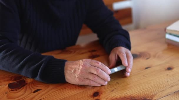 Glimlachende oude man met smartphone terwijl hij op de bank zit. — Stockvideo