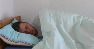 Hasta adam yatakta yatıyor ve kendini kötü hissediyor. Erkek evde dinleniyor, nezle belirtilerini hissederken kadın da alına dokunarak ateşi kontrol ediyor..