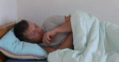 Hasta adam yüksek sıcaklıkta termometre gösteriyor. Kameraya bağlı. Evde battaniyenin altında yatıyor.
