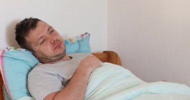 Hasta adam yatakta uzanıyor ve çok öksürüyor. Erkek kötü hissediyor ve öksürüyor.