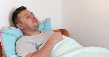 Hasta adam yatakta uzanıyor ve çok öksürüyor. Erkek kötü hissediyor ve öksürüyor.