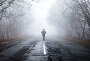 Sisli sisli yolda dramatik bir şekilde yürüyen tek adam. Sisli bir sonbahar manzarasında yürüyen bir adam
