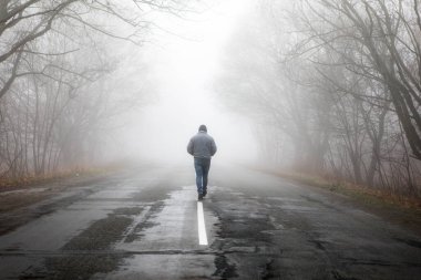 Sisli sisli yolda dramatik bir şekilde yürüyen tek adam. Sisli bir sonbahar manzarasında yürüyen bir adam