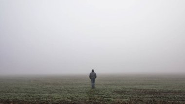 Sisli sisli yolda dramatik bir şekilde yürüyen tek adam. Sisli bir sonbahar manzarasında yürüyen bir adam