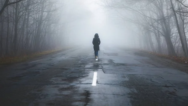孤独な女が霧の中を歩く 朝の霧の中で道路と農村風景 暖かい秋の色 暗い神秘的な背景 — ストック写真