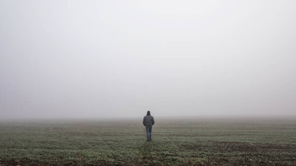 Только человек уходит на туманную туманную дорогу в драматической мистической сцене. Парень ходит по туманному осеннему пейзажу