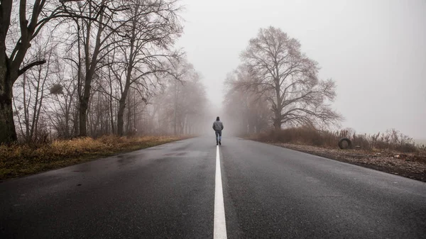 男だけが離れて劇的な神秘的なシーンで霧霧の霧の道に歩いてください 男は霧に包まれた秋の風景の中を歩く — ストック写真