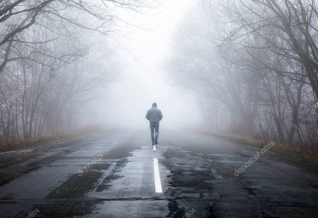 Lonly man  walk away into the misty foggy road in a dramatic mystic scene. Guy walking in a foggy autumn landscape