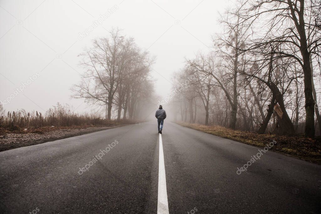 Man walking in a foggy autumn landscape. Lonely man walking in fog. Rural landscape with road in morning mist. Warm autumn colors. Dark mysterious background