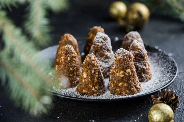 Delicious no bake chocolate  Christmas dessert healthy energy pine cone, sprinkled with powdered sugar. Decorated with fir branches. Healthy Vegan dessert