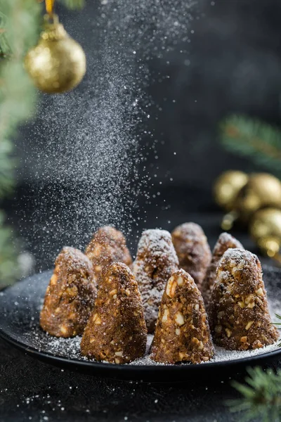 Delicious no bake chocolate  Christmas dessert healthy energy pine cone, sprinkled with powdered sugar. Decorated with fir branches. Healthy Vegan dessert