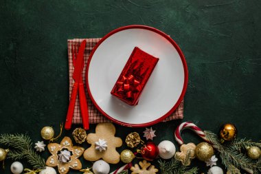 Noel ve yeni yıl sofrası. Çatal bıçaklı beyaz tabak ve Noel ağacı dalları, kırmızı beton arka planda kırmızı peçete..