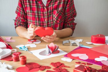 Kırmızı kağıt kalpli DIY tatil kartı, aşkın sembolü. Kız Anneler Günü 'nü, Sevgililer Günü' nü, tebrik kartını hazırlar. Hobi, sanat konsepti, kendi ellerinle hediye.