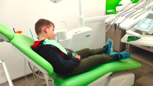 Niño sentado en la silla del dentista, pulgar hacia arriba. Concepto de odontología y medicina infantil — Vídeos de Stock