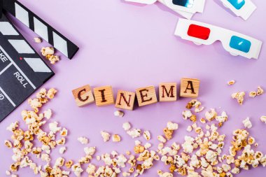 the word cinema, popcorn, clapperboard, 3D glasses and tickets top view flat lay on purple background