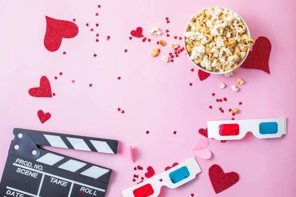 St. Valentine\'s day Movie night concept. Popcorn, 3d glasses clapper board on pink  background. Cozy holiday plans for lovers