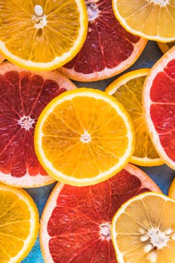 Dilimler, parçalar, bütün olgun sitruslar arka planda. Sulu mandalinalar, portakallar, greyfurtlar, limonlar, limonlar, sarı tuvalde yapraklar var. Meyve suyu hazırlamak için yaz mevsimi egzotik tropikal meyveleri.