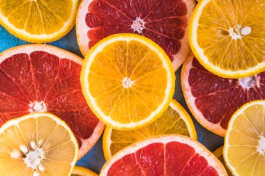 Dilimler, parçalar, bütün olgun sitruslar arka planda. Sulu mandalinalar, portakallar, greyfurtlar, limonlar, limonlar, sarı tuvalde yapraklar var. Meyve suyu hazırlamak için yaz mevsimi egzotik tropikal meyveleri.