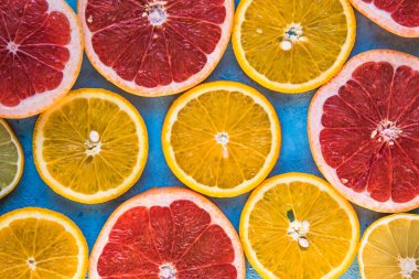 Dilimler, parçalar, bütün olgun sitruslar arka planda. Sulu mandalinalar, portakallar, greyfurtlar, limonlar, limonlar, sarı tuvalde yapraklar var. Meyve suyu hazırlamak için yaz mevsimi egzotik tropikal meyveleri.