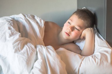 7 yaşında bir çocuk yatağında yatıyor, uykulu bir çocuk sabah uykusunda uyanıyor, üzgün bir çocuk odada bir yatakta yatıyor.