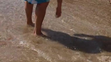 Kumlu bir sahilde deniz suyunda duran bir adamın bacakları. Suya dokunan kişi