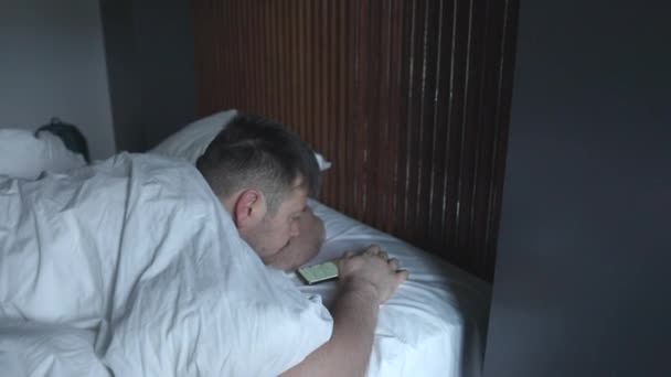 Hombre usando el teléfono móvil, navegar por Internet y mensajes de texto en el teléfono acostado en la cama — Vídeos de Stock