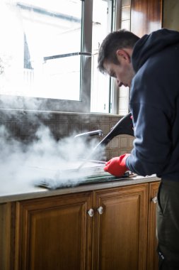 Gloved cleaner washing oven with steamer at home closeup