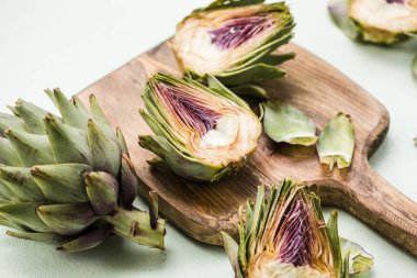 Beyaz ahşap arka planda taze enginar ve güzel bir gün ışığı gölgesi var. Yaklaş. Çiğ organik enginar çiçekleri kes