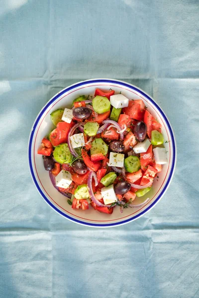 フェタチーズとギリシャのサラダ オリーブ トマト キュウリと赤玉ねぎ 健康的なベジタリアン地中海料理 低カロリーの食事 青い生地の背景 トップビュー — ストック写真