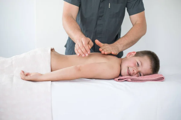 男孩蹒跚学步从治疗性按摩中放松下来 在诊所与病人打交道以治疗儿童背部的理疗师 — 图库照片