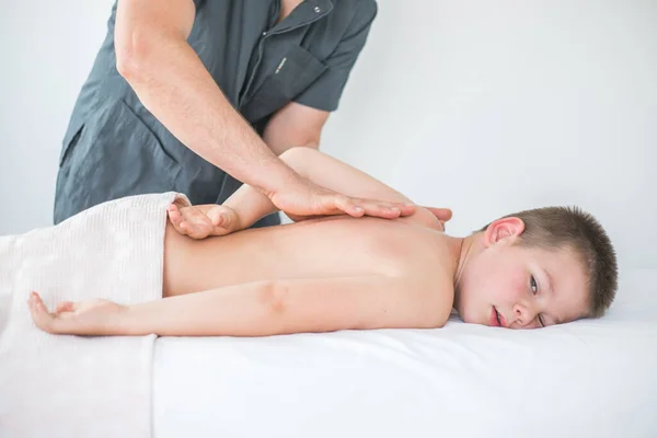 男孩蹒跚学步从治疗性按摩中放松下来 在诊所与病人打交道以治疗儿童背部的理疗师 — 图库照片