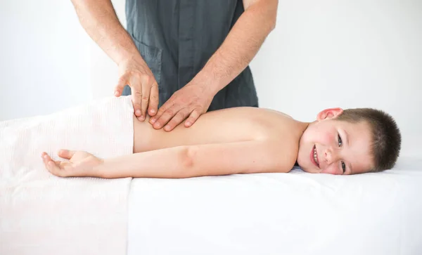 男の子幼児は治療マッサージからリラックスします 小児の背中を治療するために診療所で患者と一緒に働く理学療法士 — ストック写真