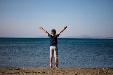 Çocuk yaz tatilinde plajda oynuyor. Doğadaki çocuklar, deniz suyunda akan kumlar ve mavilikler..