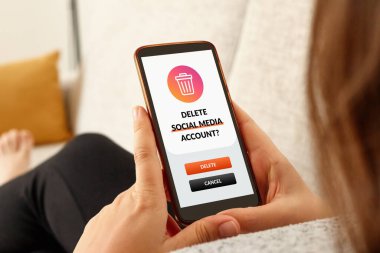 Akıllı telefonlu bir kanepede sosyal medya hesabını silen bir kızın yakın çekimi..