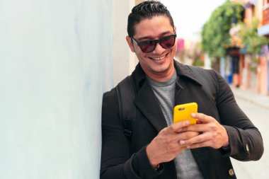 İspanyol adam sokakta cep telefonuyla yürüyor.