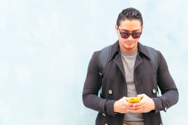 Genç adam cep telefonuyla sokakta yürüyor.