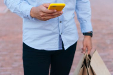 Elinde alışveriş çantaları ve cep telefonu olan tanınmayan bir adam şehir merkezinde yürüyor..