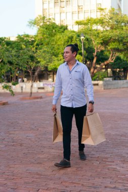 Genç adam açık havada kağıt alışveriş torbalarıyla yürüyor.