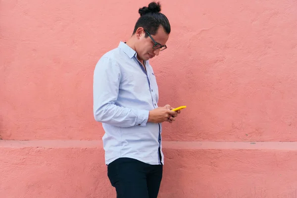 Man standing checking cell phone in front of pink wall