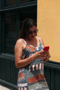 Uzun saçlı ve gözlüklü İspanyol kadın şehir sokaklarında yürüyor ve cep telefonuna doğru bakıyor..