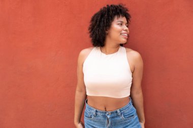 Sokakta turuncu duvarın önünde kıvırcık saçlı bir afro kadın.