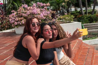 Park 'ta surat yaparken selfie çeken üç genç kız arkadaş.