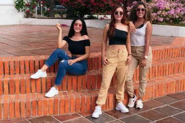 Üç Latin arkadaş parkta kameraya poz veriyor ve kameraya bakıyor..