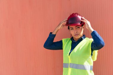 Yansıtıcı yelek giyen ve fabrikada kaskı olan kendine güvenen bir kadının portresi.