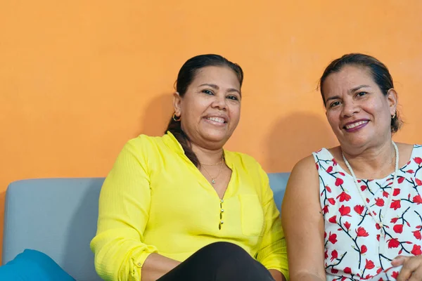 İki yetişkin kız kardeş evdeki kanepede birlikte oturuyorlar.