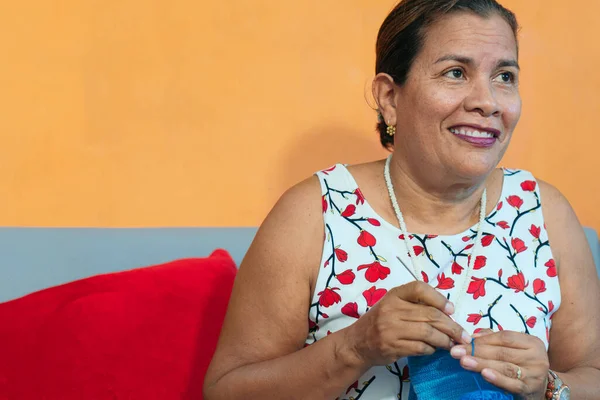 Kanepede oturan ve örgü ören Latin kadının portresi.