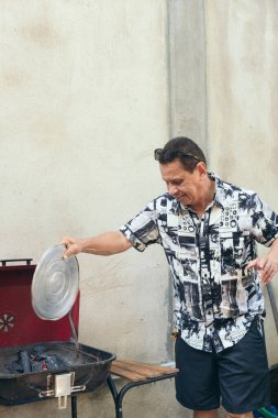 Arka bahçesinde durup ailesi için barbeküde yemek pişiren bir baba..